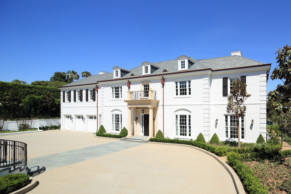 Esempio della facciata di una casa grande bianca classica a tre piani con rivestimento in mattoni e falda a timpano