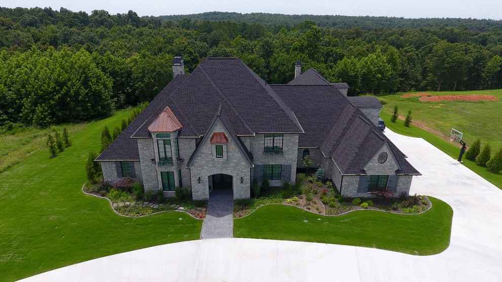 Example of a large classic gray two-story stone house exterior design in Other with a hip roof and a shingle roof