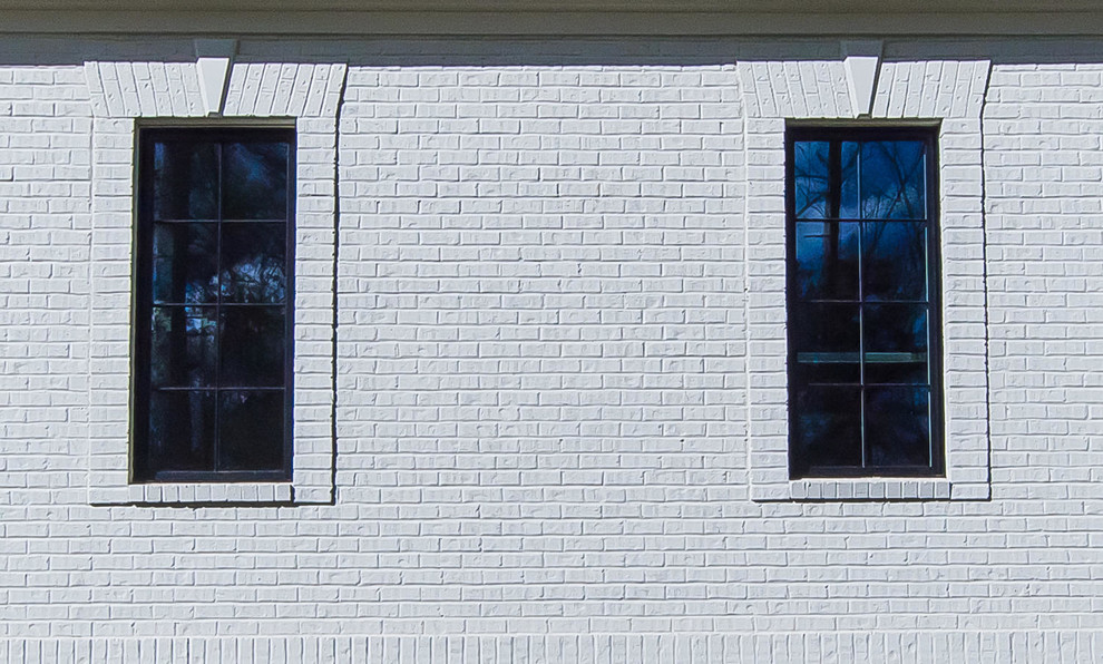 Cette photo montre une façade de maison blanche chic en stuc de taille moyenne et à un étage avec un toit à croupette et un toit en tuile.