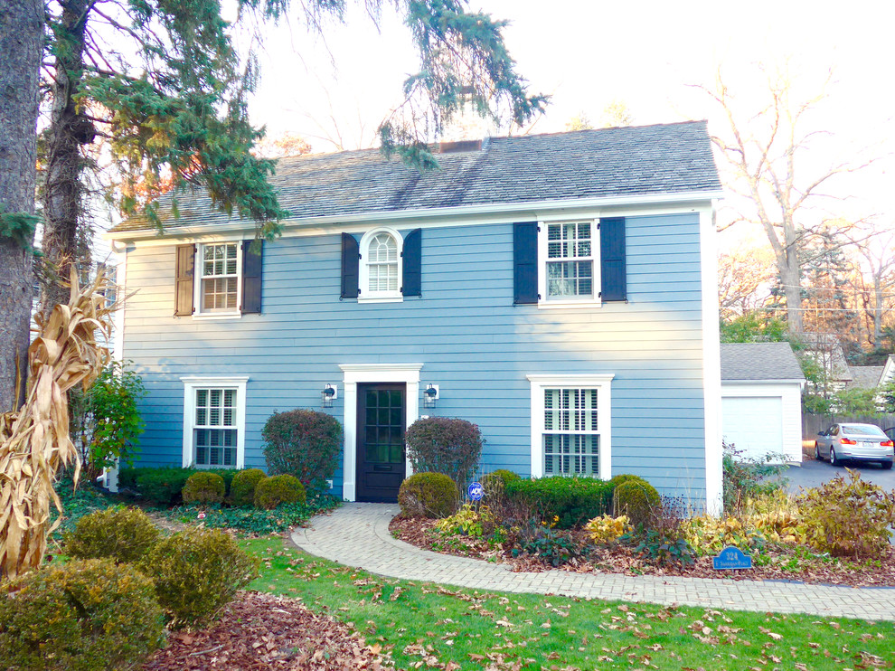 Modelo de fachada de casa azul clásica de tamaño medio de dos plantas con revestimiento de aglomerado de cemento, tejado a dos aguas y tejado de teja de madera