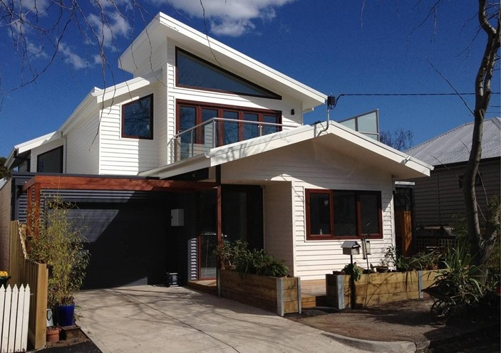 Réalisation d'une petite façade de maison blanche design en panneau de béton fibré à un étage avec un toit à deux pans et un toit en métal.