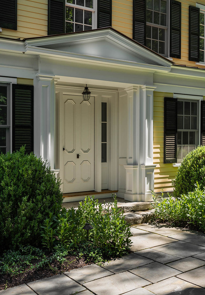 Mittelgroßes, Zweistöckiges Klassisches Einfamilienhaus mit Vinylfassade, gelber Fassadenfarbe, Schindeldach und Walmdach in Bridgeport