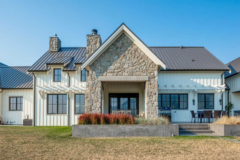 Esempio della villa grande bianca country a due piani con rivestimento con lastre in cemento, tetto a capanna e copertura in metallo o lamiera