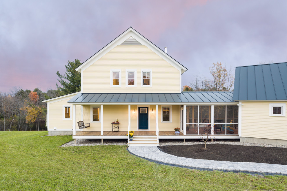 Immagine della villa gialla country a due piani con rivestimento in legno, tetto a capanna e copertura in metallo o lamiera