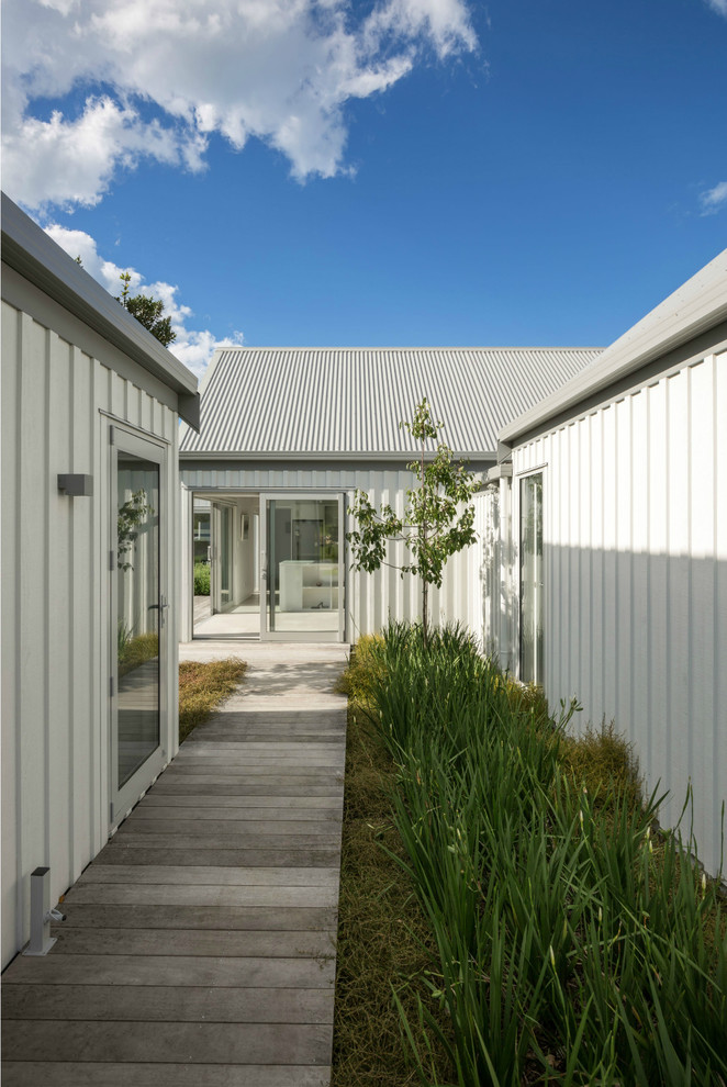 Идея дизайна: одноэтажный, белый частный загородный дом среднего размера в стиле лофт с облицовкой из металла, двускатной крышей и металлической крышей