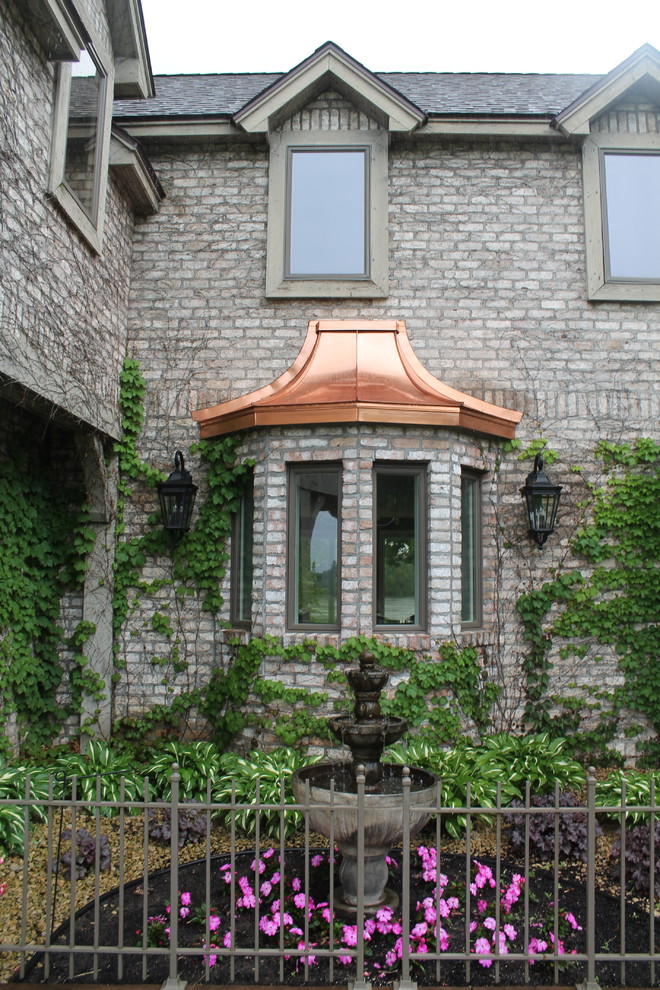 Imagen de fachada gris clásica grande de dos plantas con revestimiento de ladrillo y tejado a dos aguas