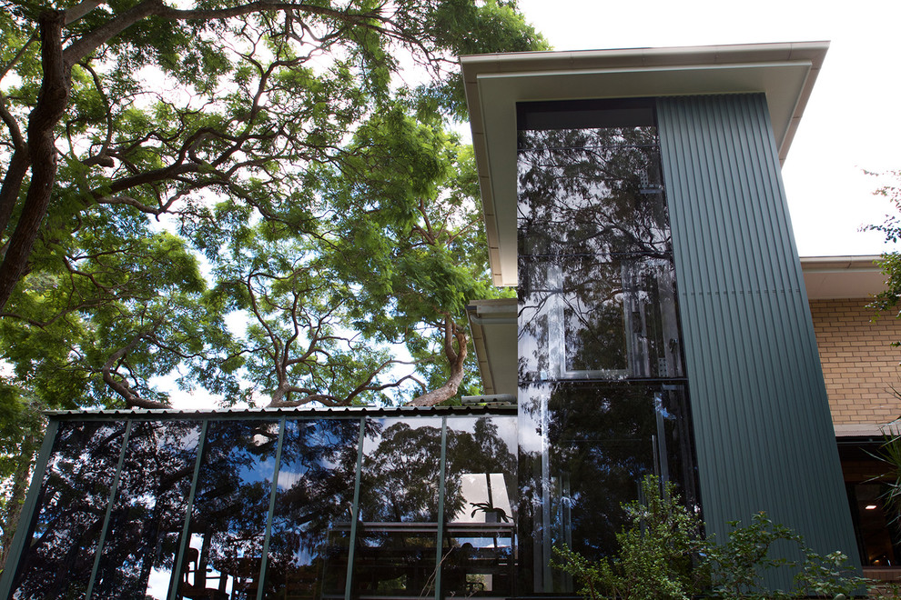 Cette image montre une grande façade de maison verte design en verre à un étage avec un toit en métal.