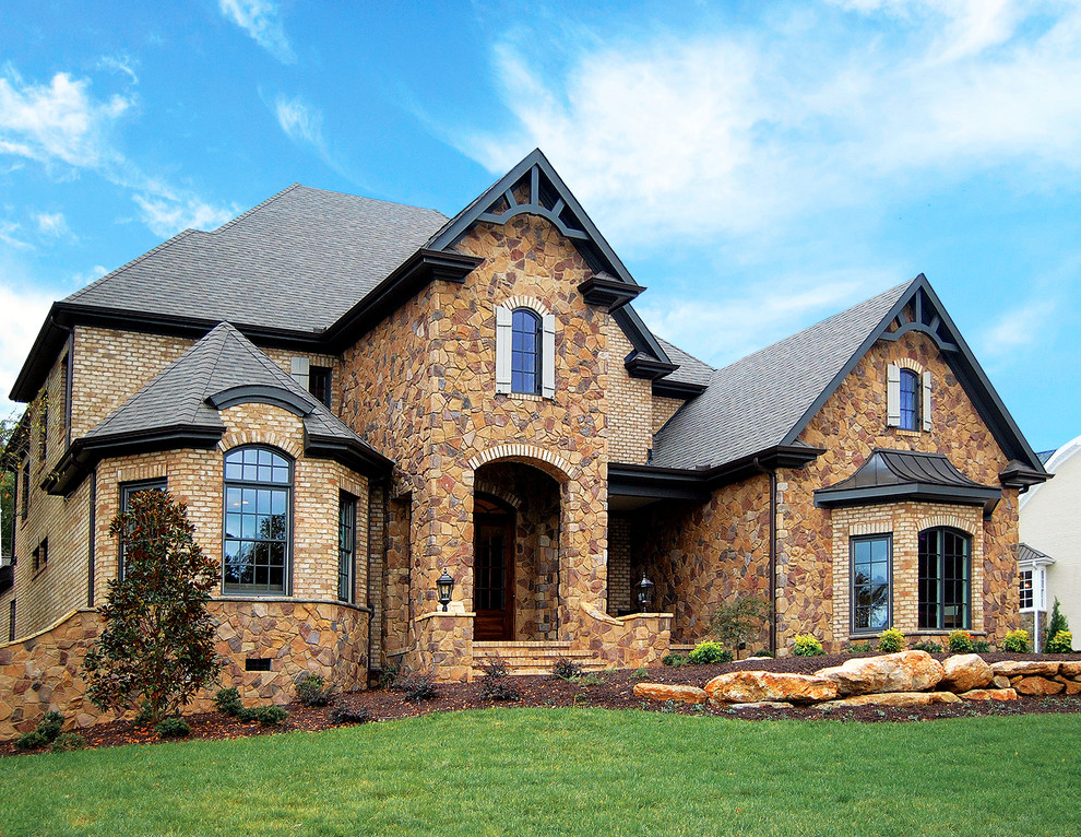 Large arts and crafts multicolored two-story stone house exterior photo in Charlotte with a hip roof and a shingle roof