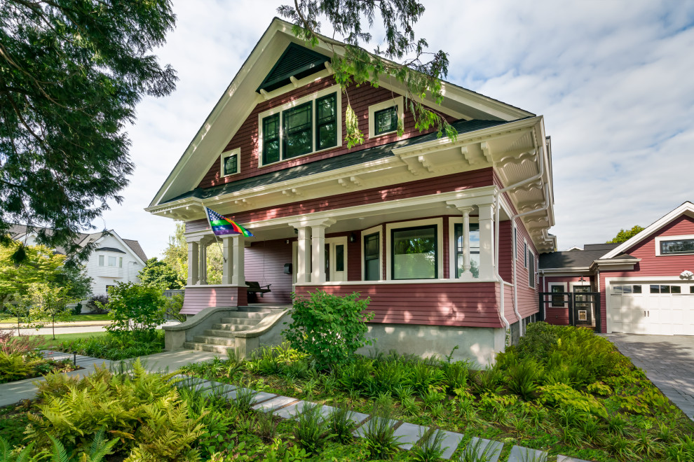 Esempio della villa grande rossa american style a due piani con rivestimento in legno, tetto a capanna e copertura a scandole