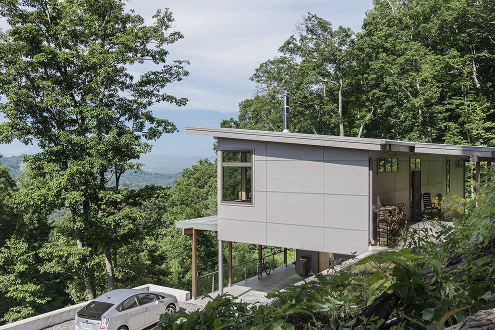 На фото: маленький, двухэтажный, серый частный загородный дом в стиле модернизм с облицовкой из бетона и односкатной крышей для на участке и в саду с