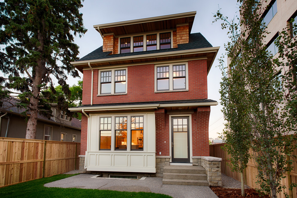 Example of a classic red three-story brick exterior home design in Calgary with a hip roof