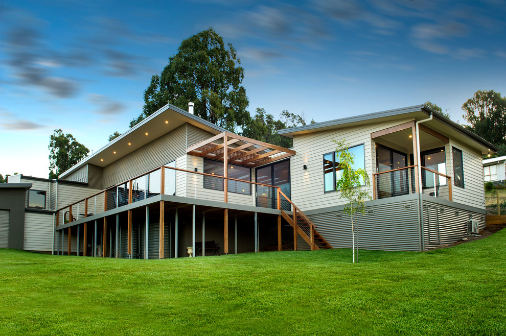 Cette image montre une façade de maison beige design en bois à un étage avec un toit en métal.