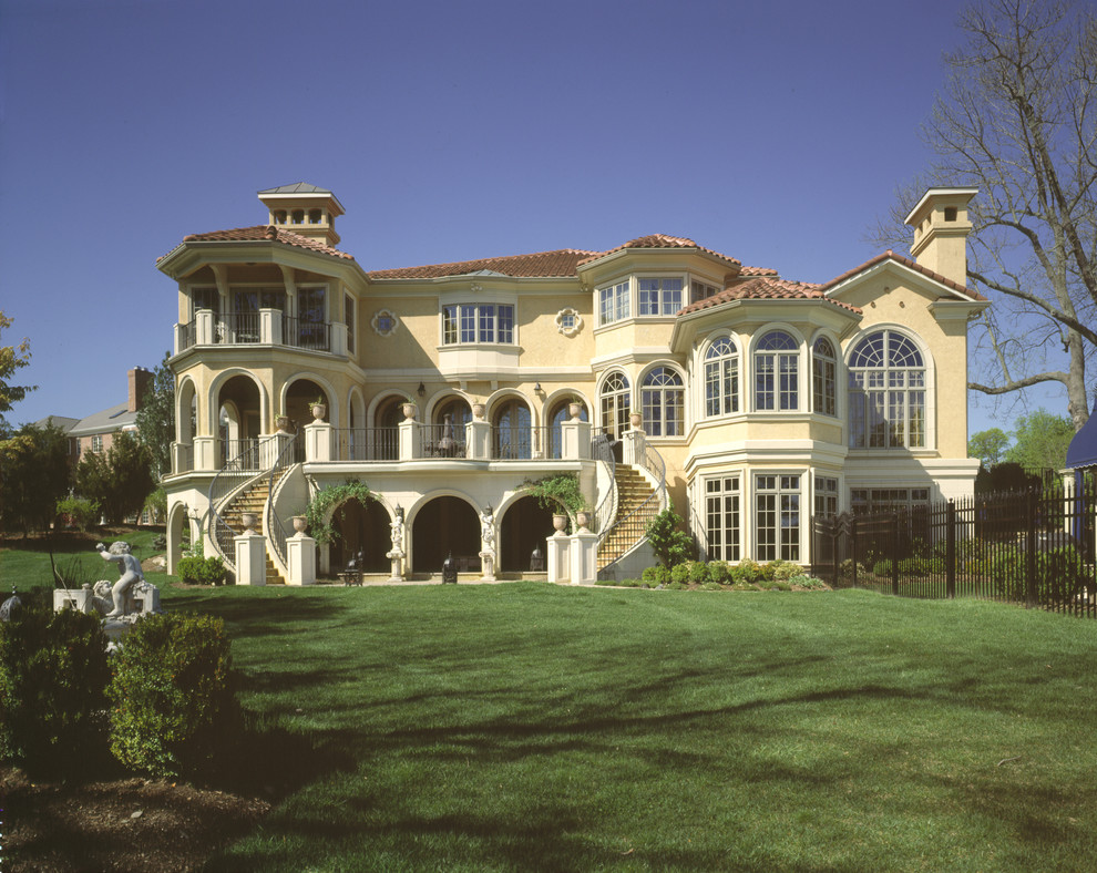 Aménagement d'une très grande façade de maison beige classique en stuc à deux étages et plus avec un toit à quatre pans.