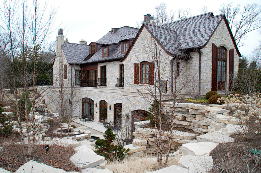 Esempio della villa ampia beige classica a tre piani con rivestimento in pietra e tetto a capanna