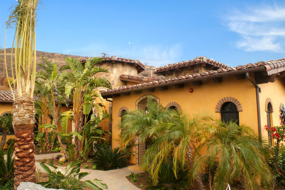 Пример оригинального дизайна: одноэтажный, оранжевый частный загородный дом в средиземноморском стиле с облицовкой из цементной штукатурки, вальмовой крышей и черепичной крышей