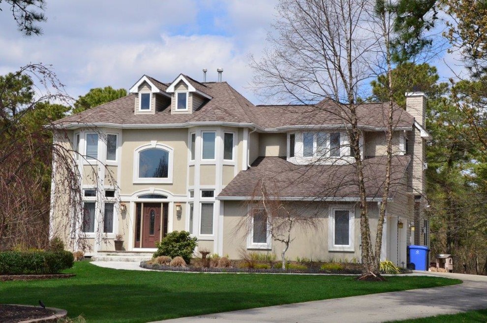 Large transitional beige two-story stucco house exterior photo in New York with a hip roof and a shingle roof