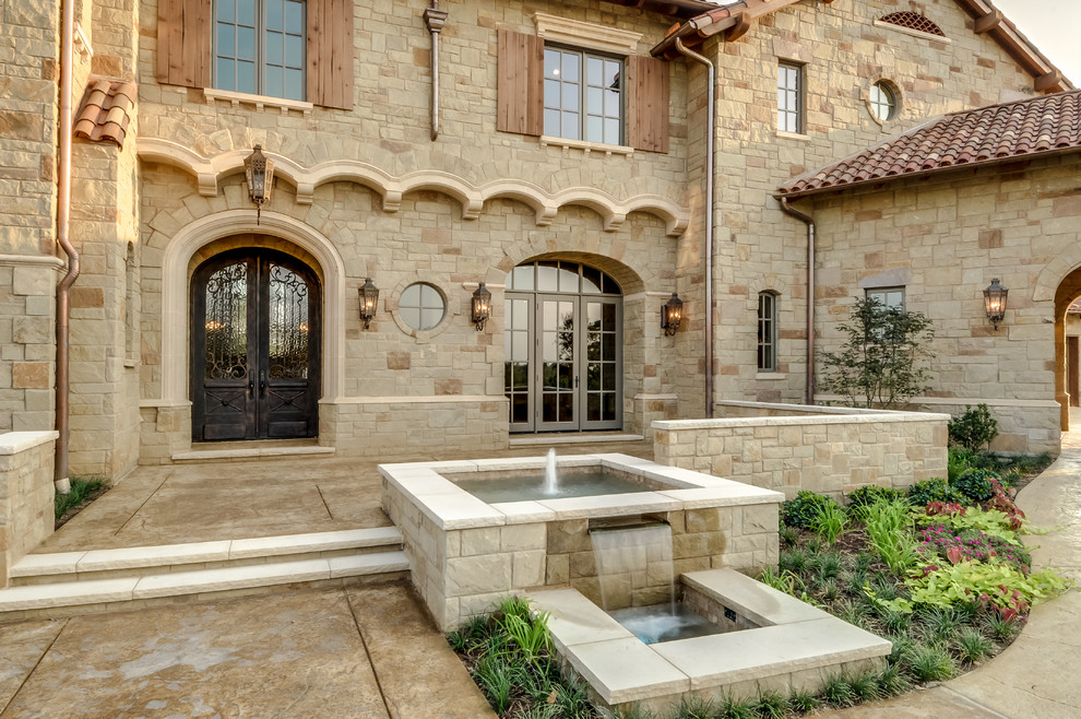 This is an example of an expansive and beige mediterranean two floor house exterior in Dallas with stone cladding and a pitched roof.