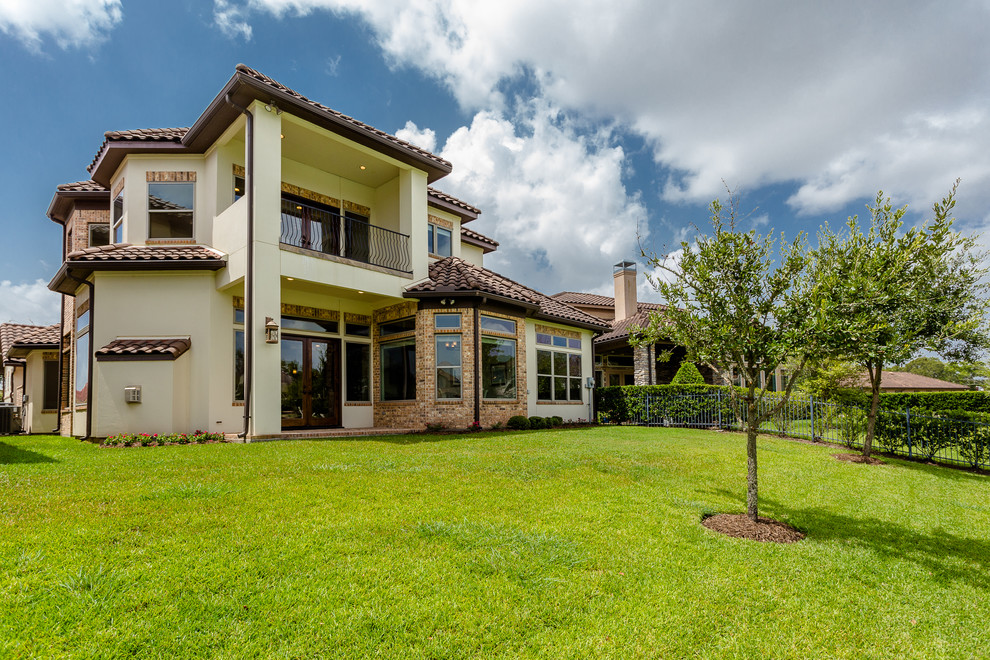 Diseño de fachada de casa beige mediterránea grande de dos plantas con revestimientos combinados, tejado a cuatro aguas y tejado de teja de barro