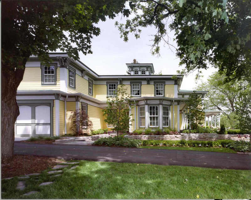 Immagine della villa ampia gialla classica a tre piani con rivestimento in legno, tetto a padiglione e copertura a scandole