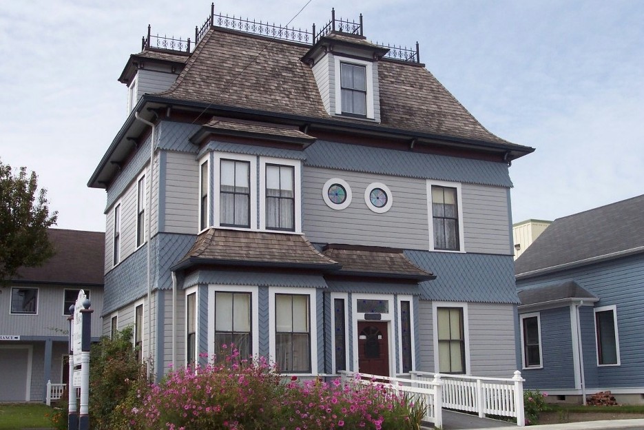 Medium sized and blue victorian house exterior in Seattle with three floors, wood cladding and a mansard roof.