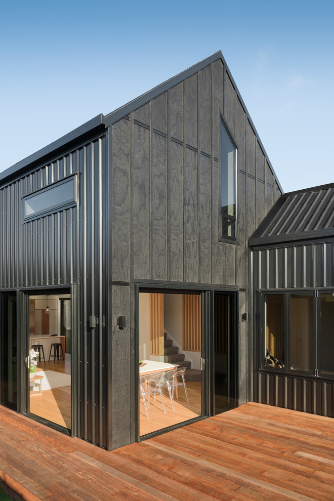 Aménagement d'une petite façade de maison de ville noire bord de mer en bois à un étage avec un toit à deux pans et un toit en métal.
