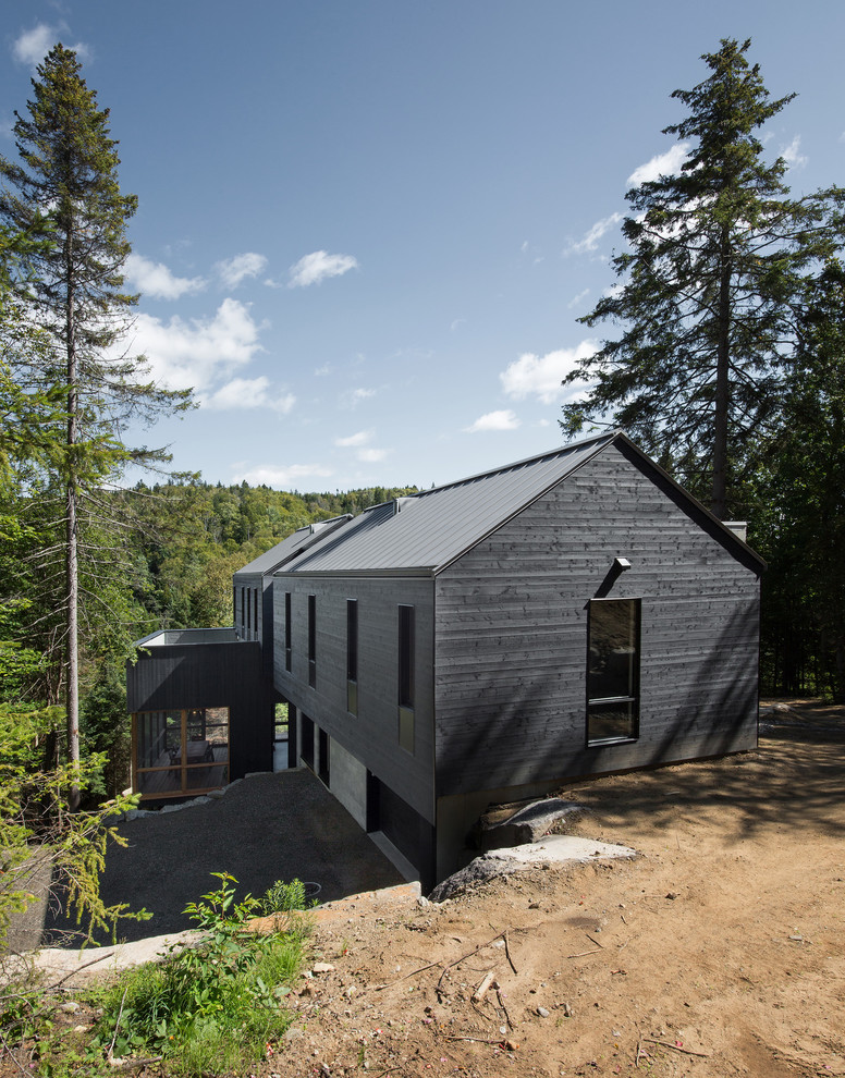 Réalisation d'une grande façade de maison noire design en bois à un étage avec un toit à deux pans et un toit en métal.