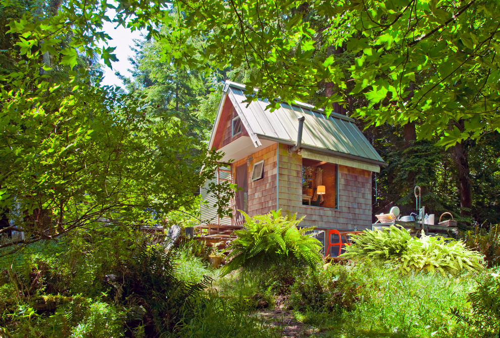 Esempio della micro casa piccola rustica a un piano con rivestimento in legno e tetto a capanna