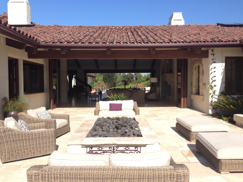Immagine di un ampio patio o portico mediterraneo dietro casa con un focolare, pavimentazioni in pietra naturale e un tetto a sbalzo