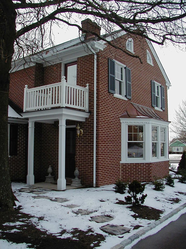 Réalisation d'une façade de maison rouge tradition en brique de taille moyenne et à un étage avec un toit à deux pans.