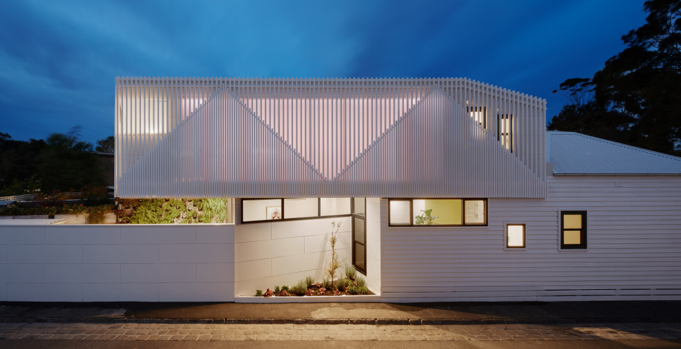 Cette image montre une petite façade de maison métallique et blanche design à un étage avec un toit plat et un toit en métal.
