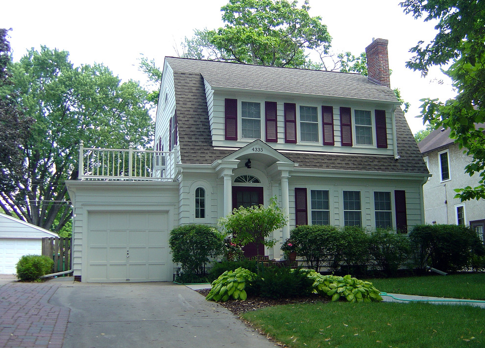 Foto della facciata di una casa piccola bianca classica a due piani con tetto a mansarda e rivestimento con lastre in cemento
