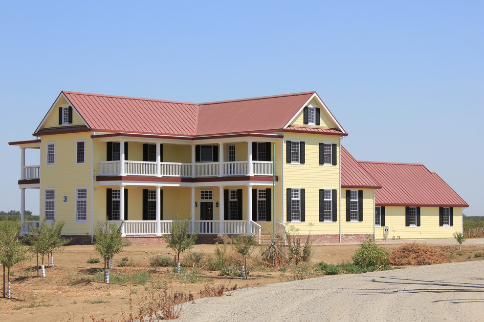 Réalisation d'une grande façade de maison jaune champêtre en panneau de béton fibré et bardage à clin à un étage avec un toit à deux pans, un toit en métal et un toit rouge.