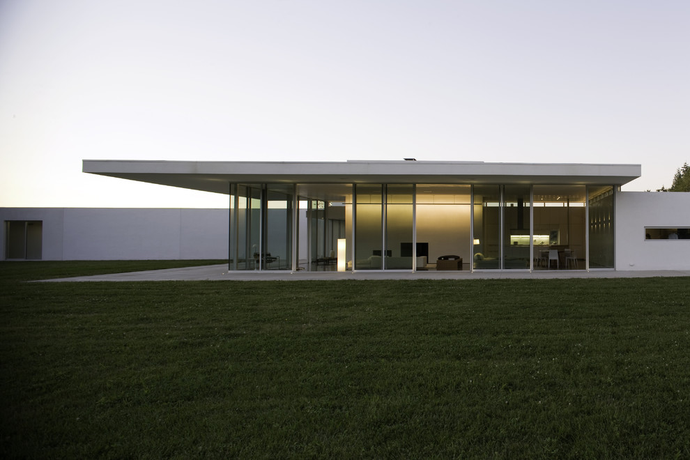 Стильный дизайн: одноэтажный, белый частный загородный дом в стиле модернизм с облицовкой из цементной штукатурки и плоской крышей - последний тренд