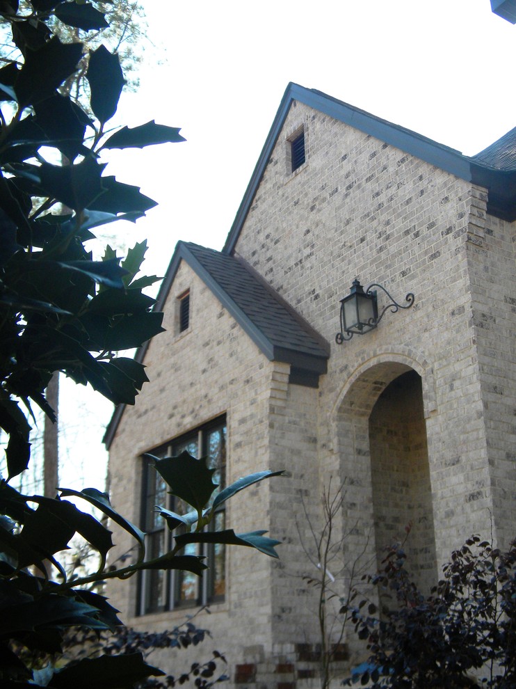 Aménagement d'une grande façade de maison beige méditerranéenne en brique à un étage avec un toit à deux pans.