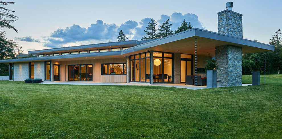 Aménagement d'une grande façade de maison grise contemporaine en béton à un étage avec un toit plat et un toit mixte.