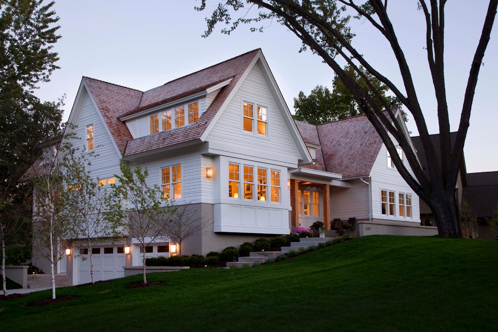 Foto della facciata di una casa bianca classica con rivestimento in legno e terreno in pendenza