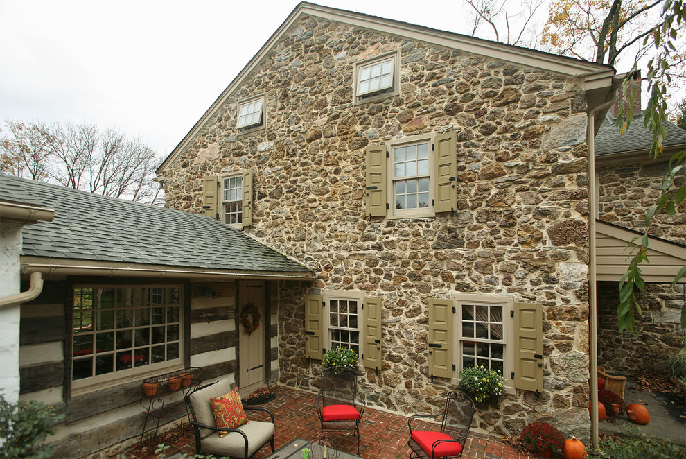 Foto della facciata di una casa piccola beige country a due piani con rivestimento in pietra e tetto a capanna