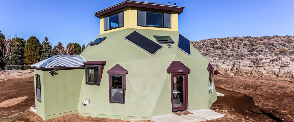 Small southwestern green two-story stucco house exterior idea in Other with a hip roof and a metal roof