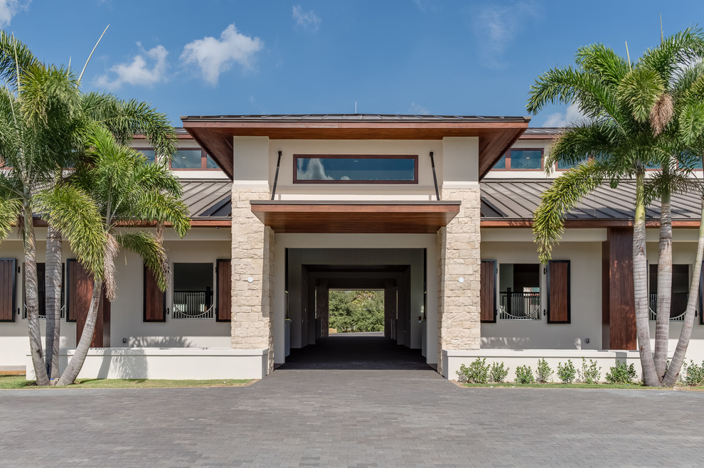 This is an example of a large and beige contemporary bungalow concrete detached house in Miami with a hip roof and a metal roof.