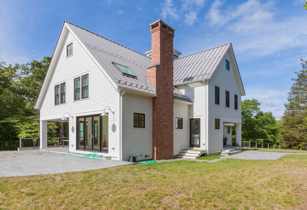 Réalisation d'une façade de maison blanche champêtre en panneau de béton fibré à deux étages et plus avec un toit à deux pans et un toit en métal.