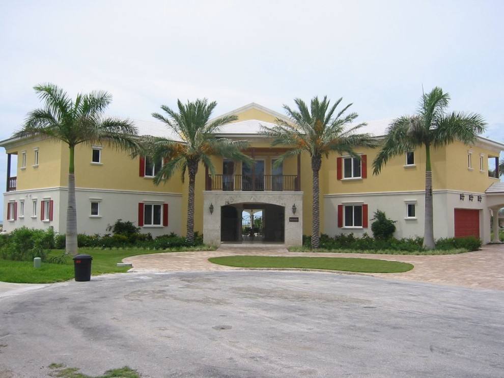 Example of a huge island style yellow three-story stucco exterior home design in Other