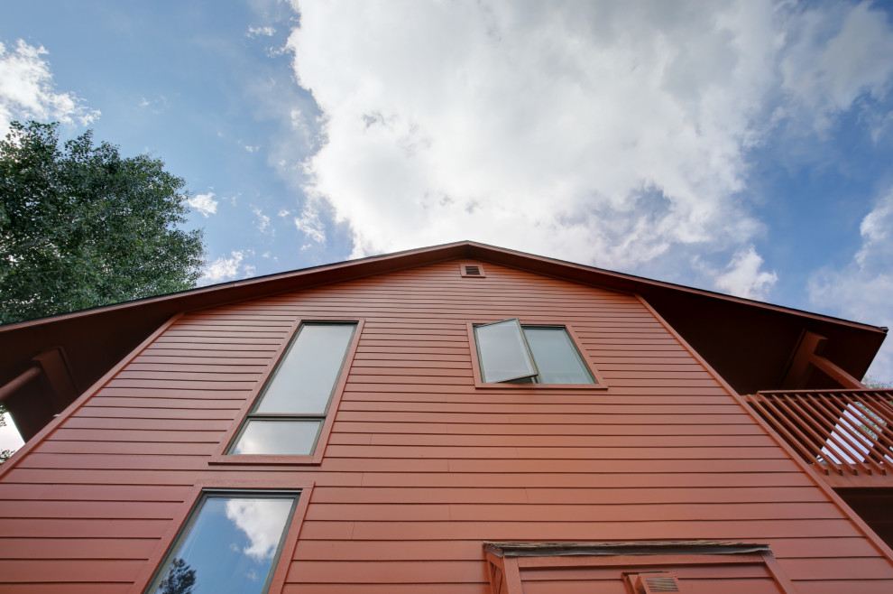 На фото: большой, трехэтажный, красный частный загородный дом в стиле рустика с облицовкой из ЦСП, двускатной крышей и крышей из гибкой черепицы с