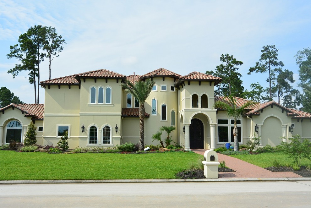 Large tuscan yellow two-story stucco house exterior photo in Houston with a hip roof and a tile roof
