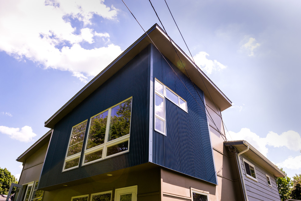 Foto på ett mellanstort funkis blått hus, med två våningar, blandad fasad, tak i metall och pulpettak