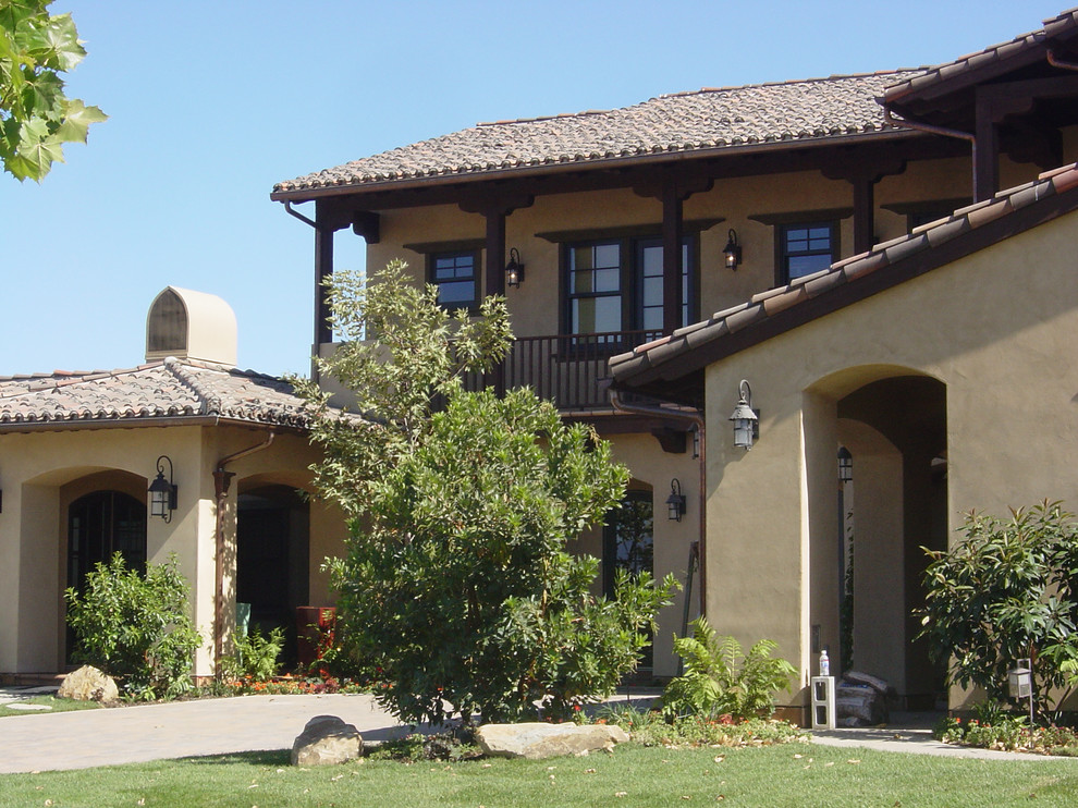 На фото: двухэтажный, бежевый дом среднего размера в средиземноморском стиле с облицовкой из цементной штукатурки и вальмовой крышей с