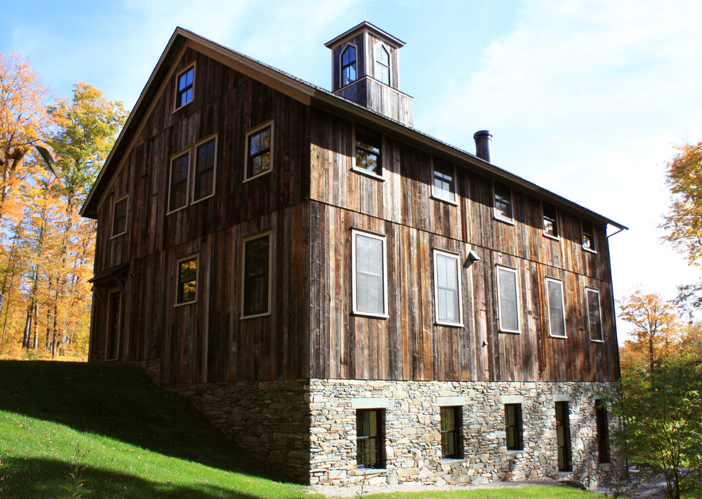 Modelo de fachada de casa beige rural grande de tres plantas con revestimiento de madera y tejado a dos aguas