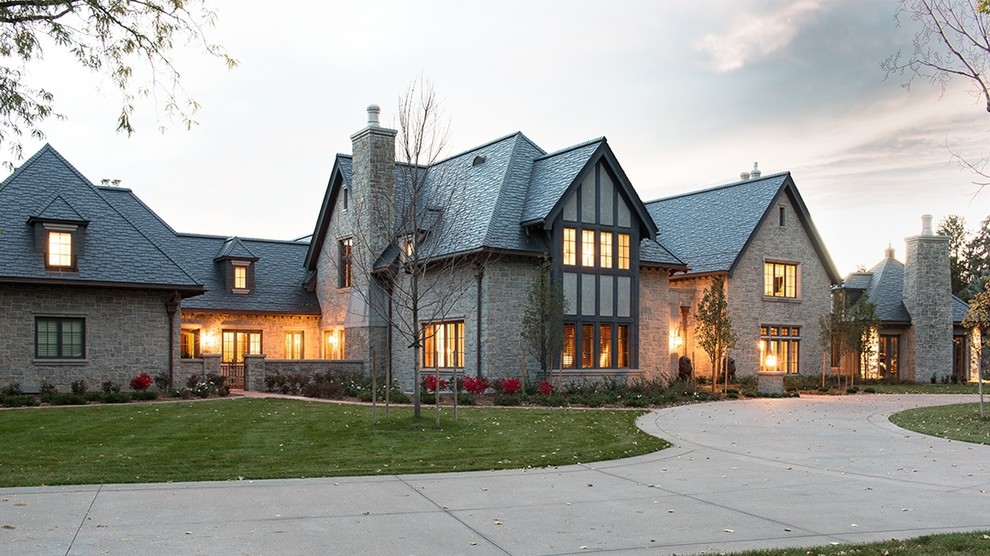 Cette image montre une très grande façade de maison grise traditionnelle en pierre à un étage avec un toit à quatre pans.