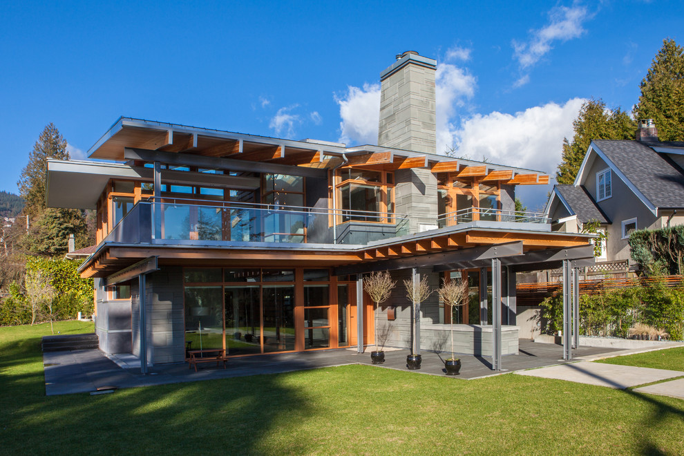 Cette image montre une grande façade de maison grise design en verre à un étage avec un toit plat.