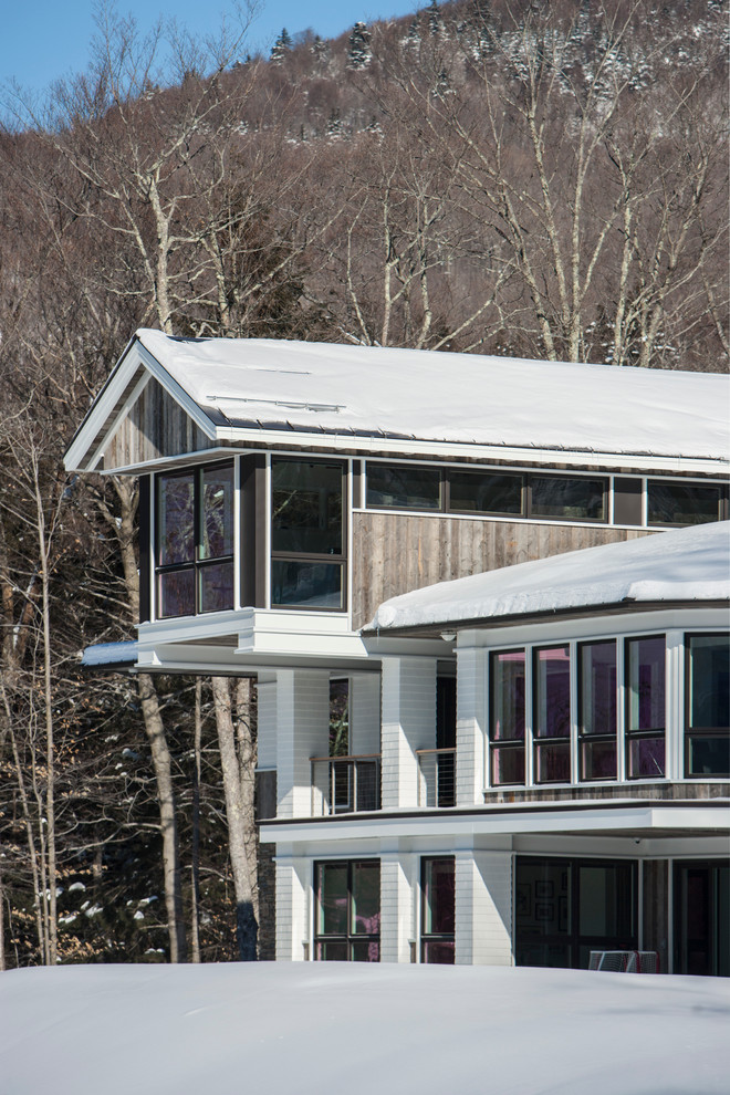 Foto della villa grande bianca contemporanea a tre piani con rivestimento in legno, tetto a capanna e copertura in metallo o lamiera
