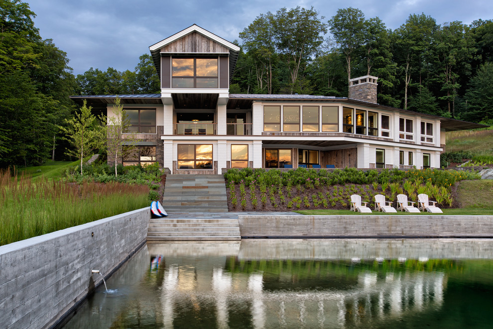 Imagen de fachada de casa blanca actual grande de tres plantas con tejado a dos aguas, revestimiento de madera y tejado de metal
